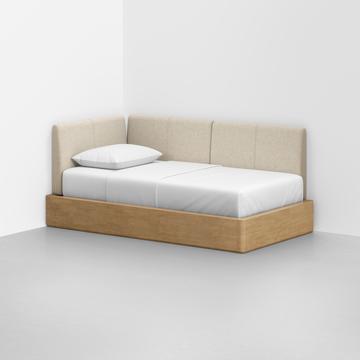 The Essential Daybed, featuring a light wood base and beige upholstered backrest, is set in the corner of a minimal white room with white bedding and a single white pillow.