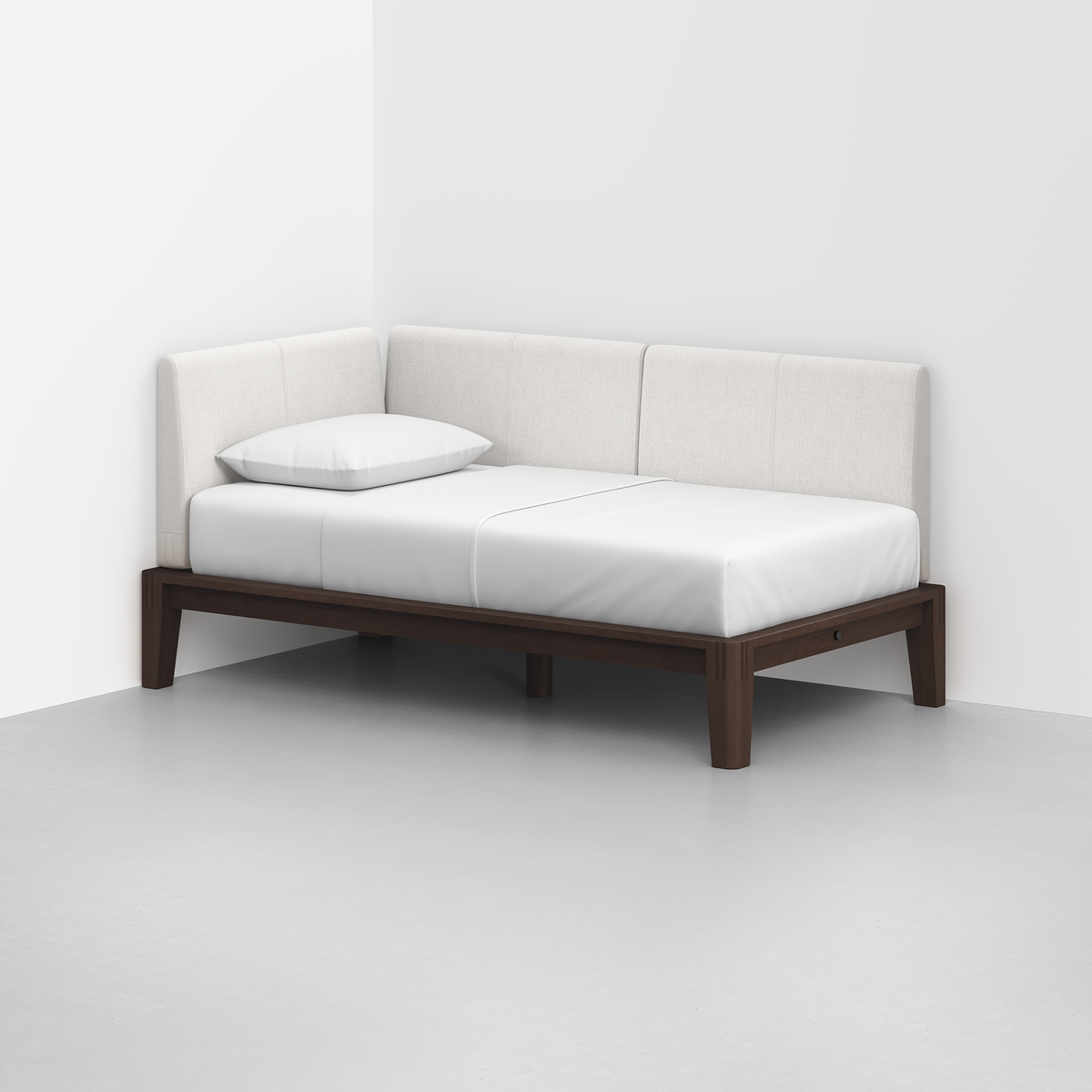 The Classic Daybed features a dark wooden frame with a white mattress, backrest, and armrest, positioned in the corner of a minimalistic room with light grey flooring and white walls.