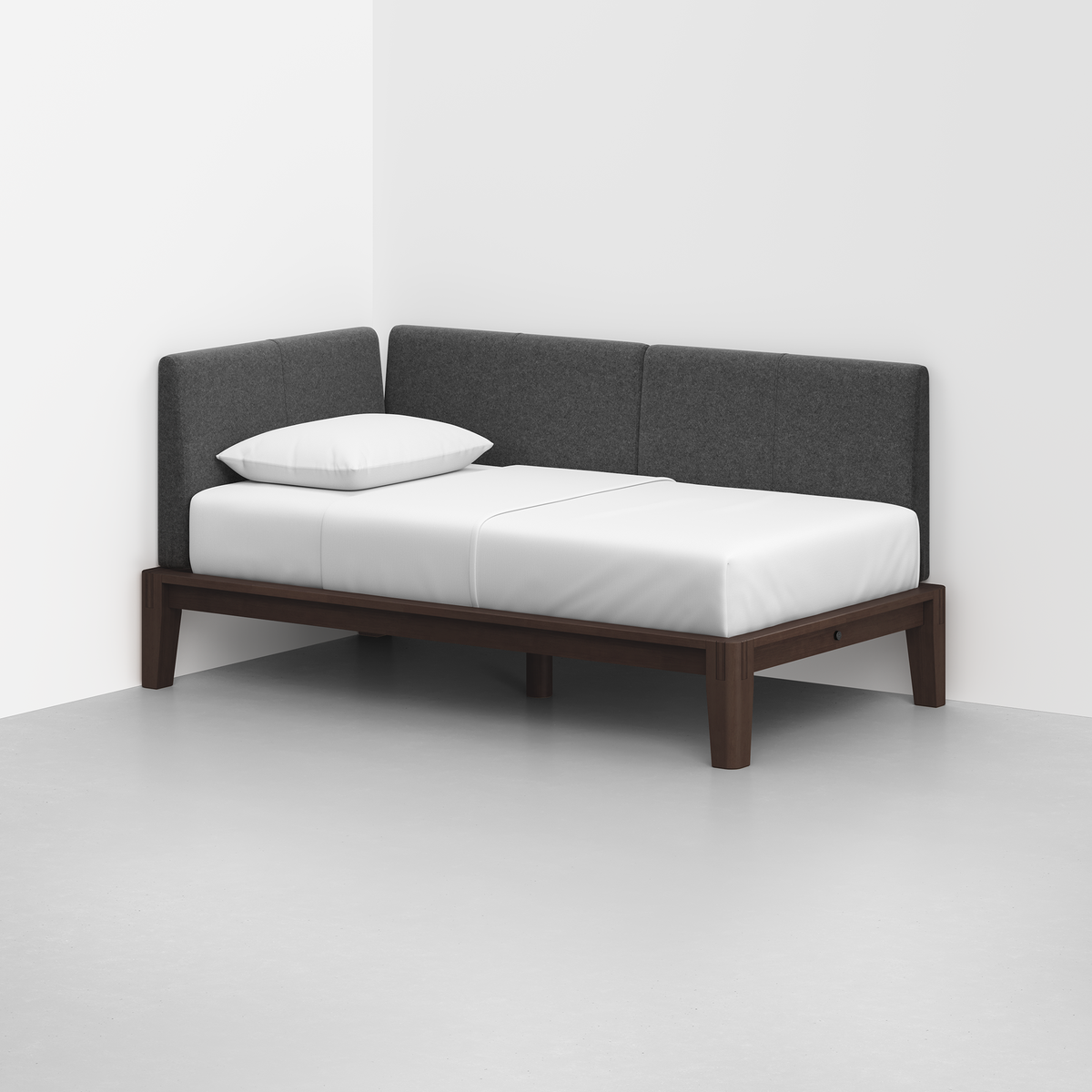 The Classic Daybed features a dark wood frame, white mattress, single white pillow, and dark gray upholstered backrest, elegantly placed in the corner of a minimalist room with white walls and a light floor.