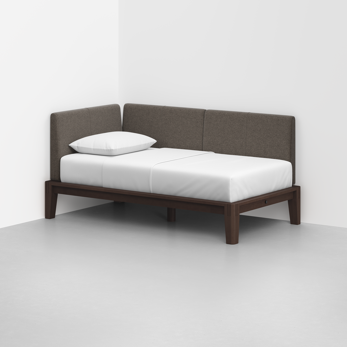 The Classic Daybed features a wooden frame, white mattress and pillow, and brown upholstered back and side panels, set in the corner of a minimalist room with white walls and a light gray floor.