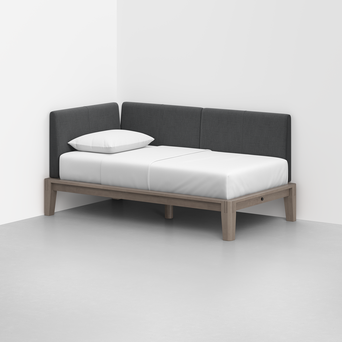 The Classic Daybed features a light wood frame, dark gray upholstered backrests, a white mattress, and a single white pillow, perfectly situated in the corner of a modern white room.