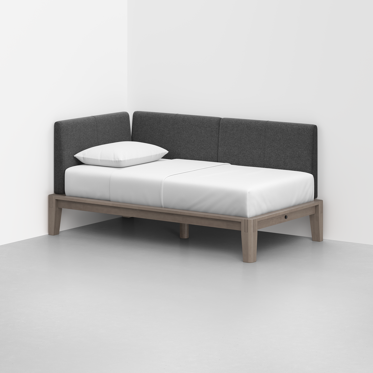 The Classic Daybed features a minimalist light wooden frame, a white mattress, and gray upholstered back and side cushions, perfectly positioned in the corner of a plain white room.