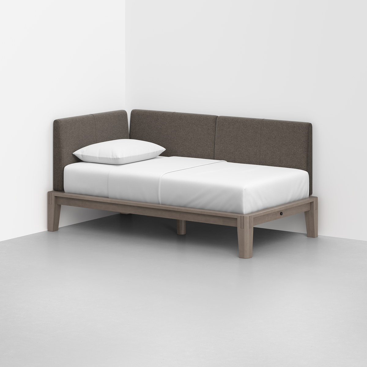 The Classic Daybed features a light gray wooden frame, white mattress and pillow, and dark gray upholstered backrests, styled in the corner of a minimalist room with white walls and a light gray floor.