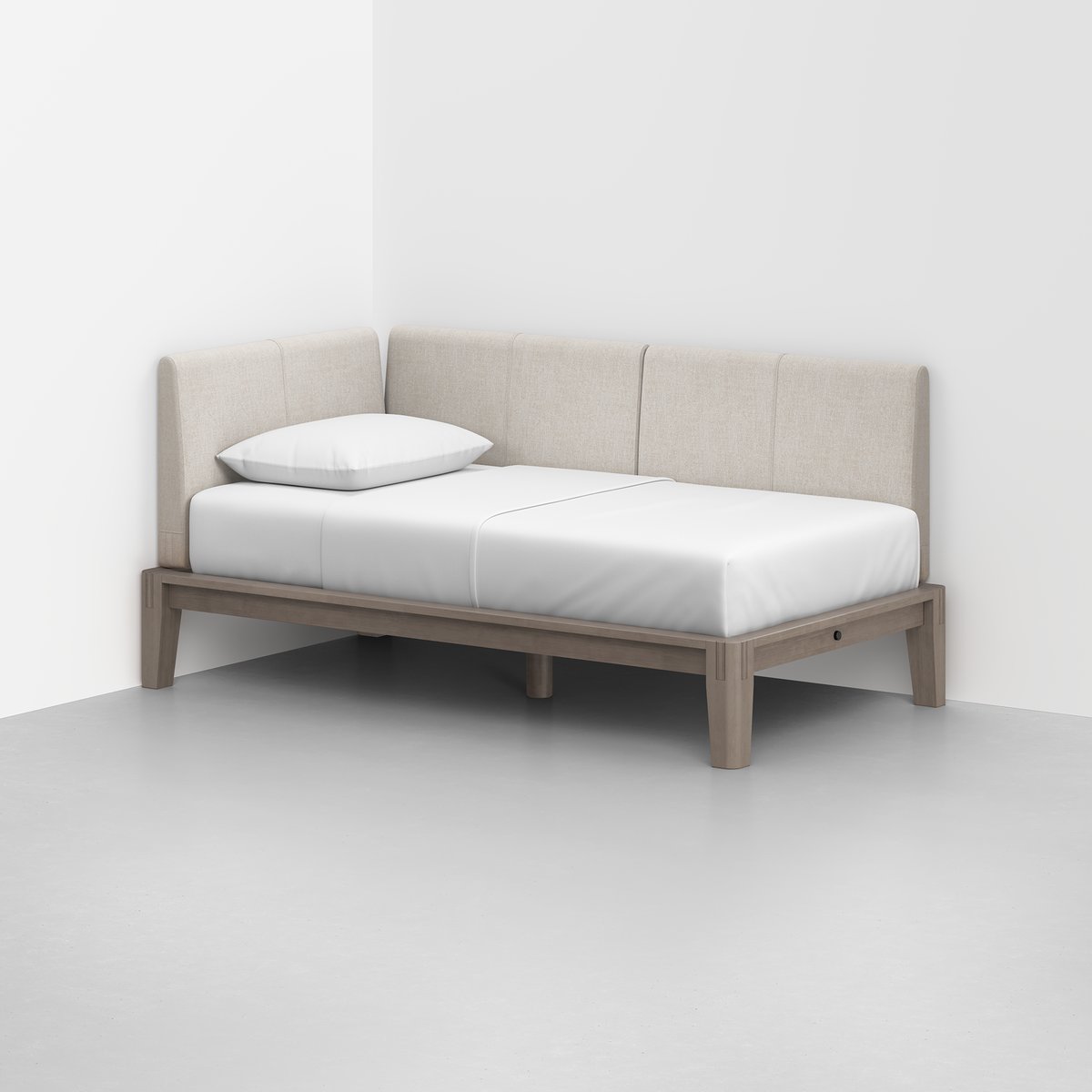 The Classic Daybed, featuring a light wood frame and beige upholstered backrests, sits in the corner of a white room. It includes a white mattress and a single white pillow.
