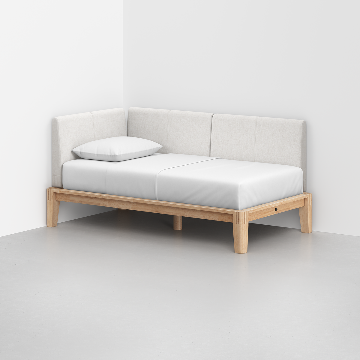 The Classic Daybed, featuring a light wooden frame, white mattress and pillow, and light gray upholstered backrests, sits in the corner of a white room.