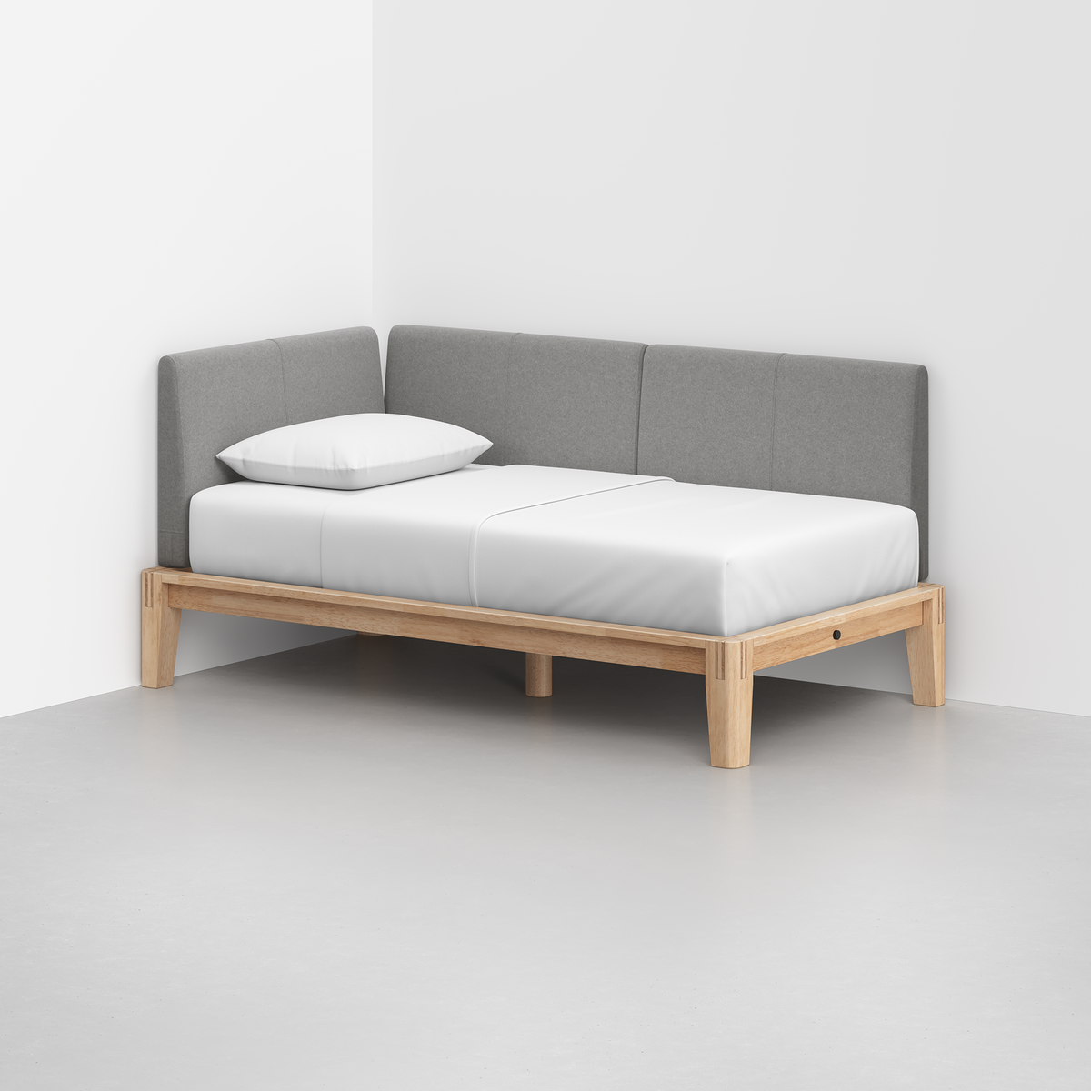 The Classic Daybed features a light wood frame, white mattress, single white pillow, and gray upholstered backrest, placed in the corner of a white room.