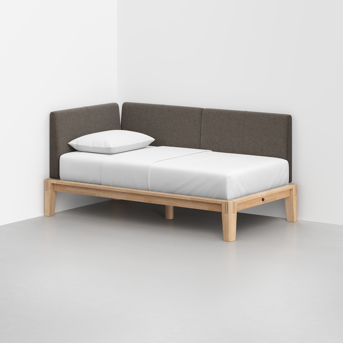 The Classic Daybed features a light wooden frame, white mattress, single white pillow, and dark gray upholstered backrest, set in the corner of a minimalist room with white walls and a gray floor.