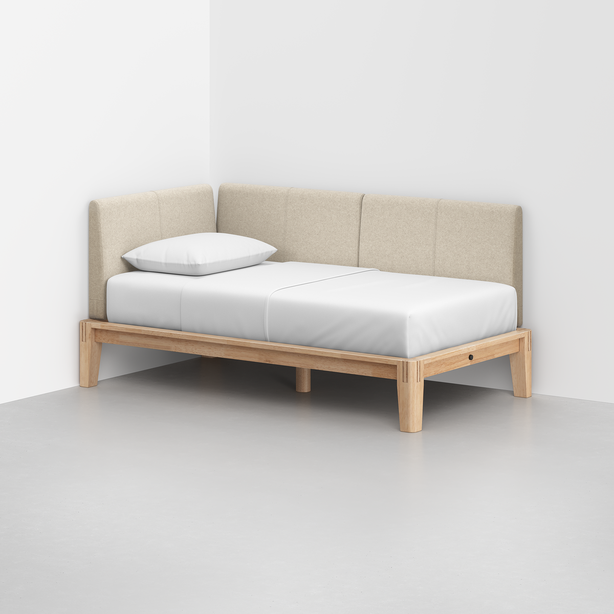 The Classic Daybed features a light wooden frame, beige upholstered backrest, white mattress, and single pillow, shown in the corner of a modern room with light gray floors and white walls.