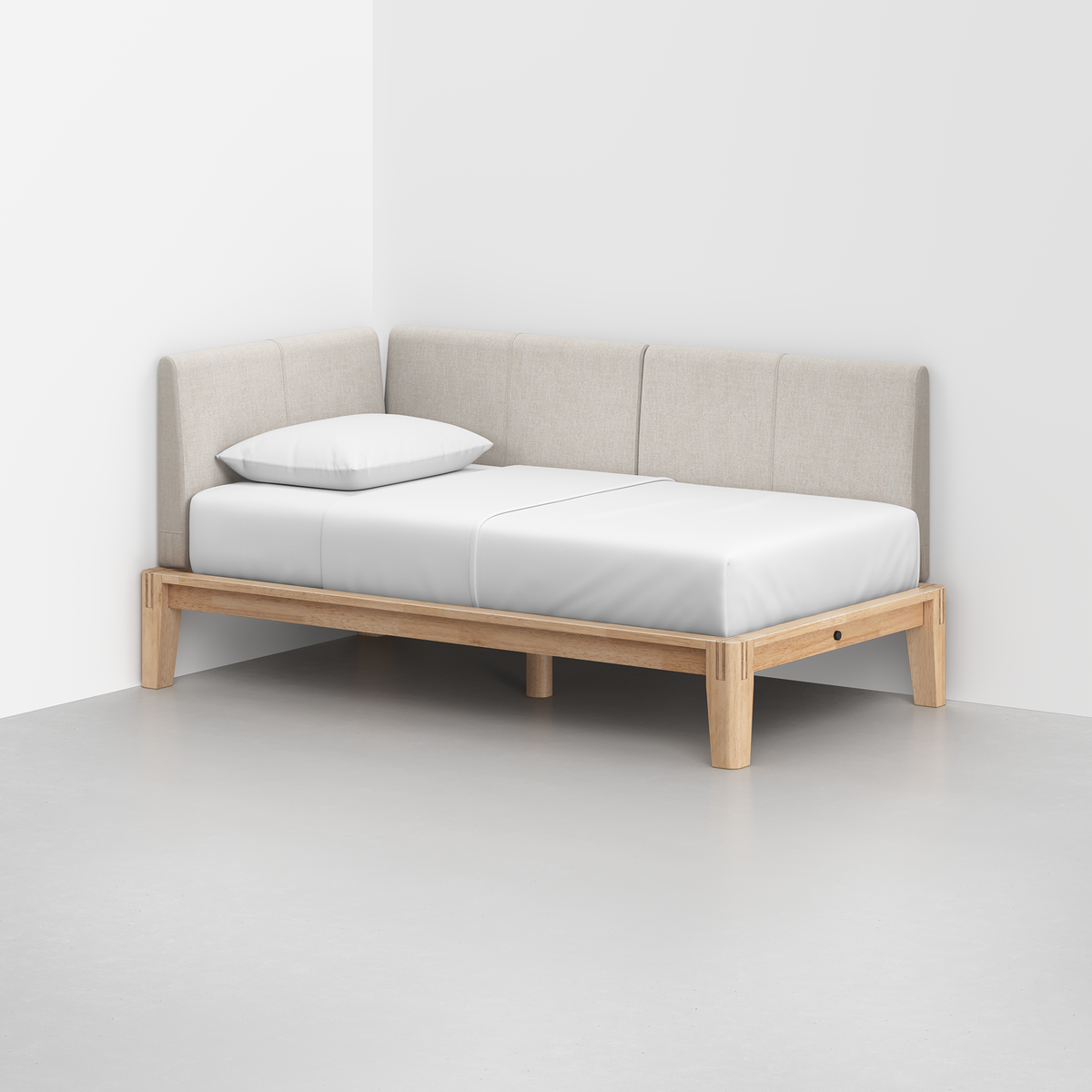 The Classic Daybed features a light wood frame, beige upholstered back and side panels, and a white mattress with a pillow, set in the corner of a minimalist room with white walls and a gray floor.