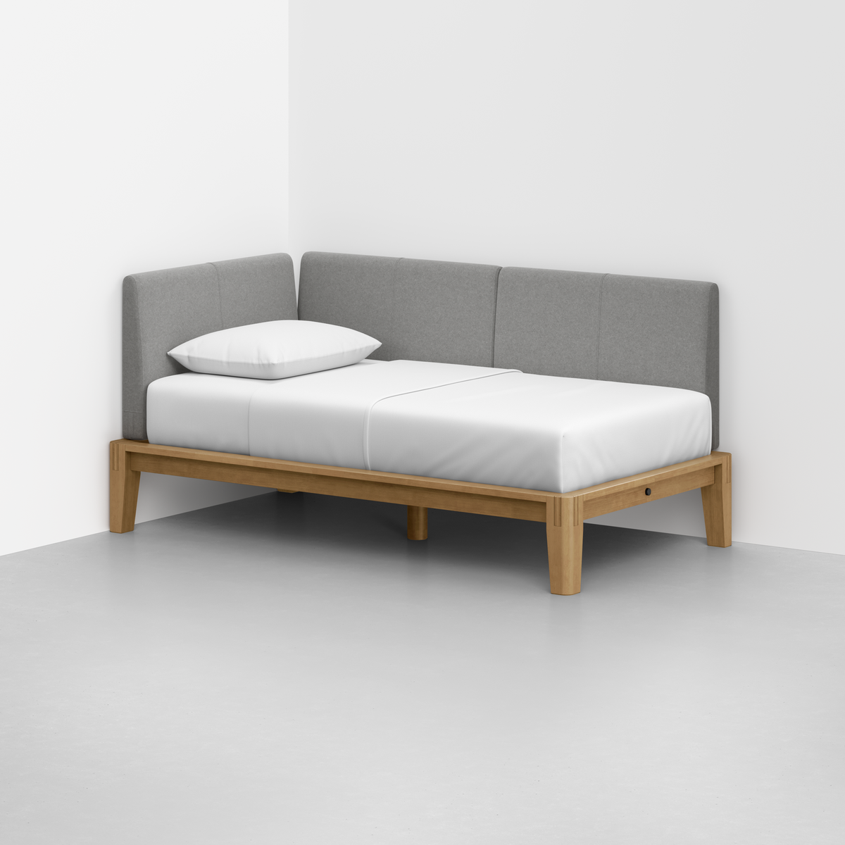 The Classic Daybed features a minimalist wooden frame, gray upholstered back and sides, a white mattress, and a single white pillow, positioned in the corner of a light-toned room.