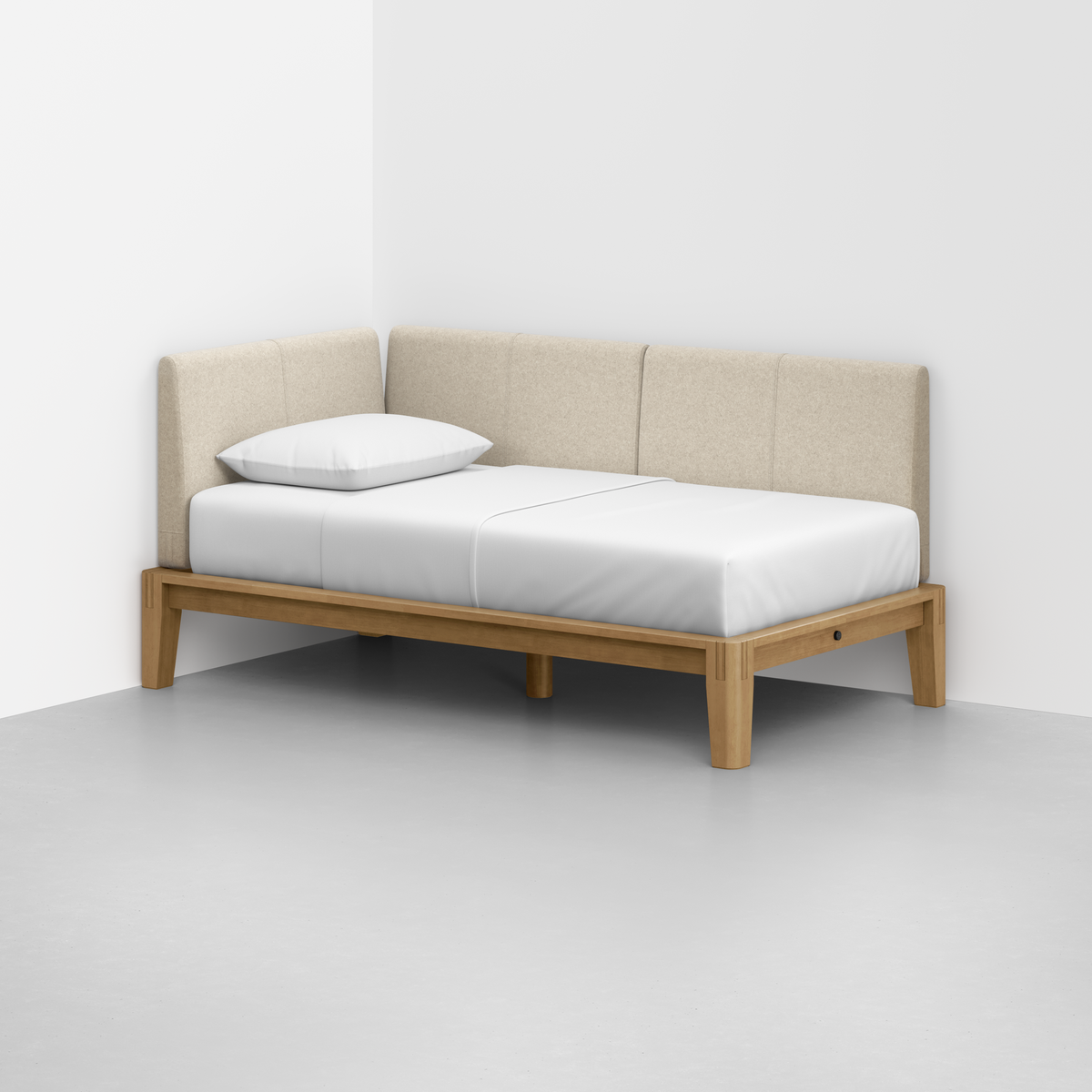 The Classic Daybed features a light wooden frame, white mattress, single white pillow, and beige upholstered backrest, positioned in the corner of a plain white room with a gray floor.