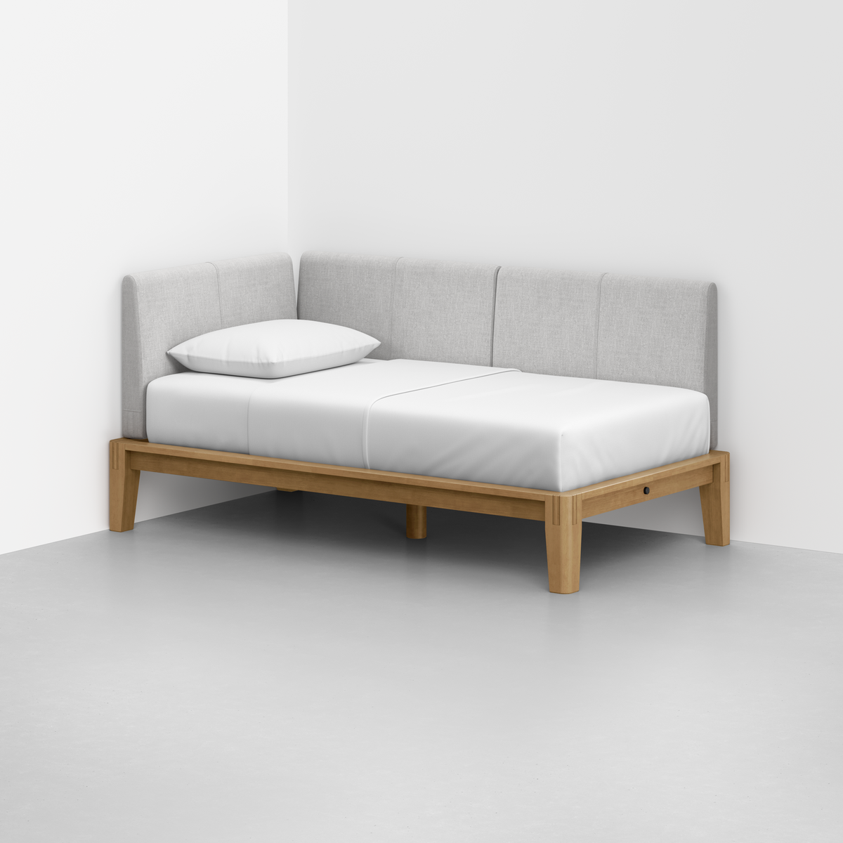The Classic Daybed features a minimalist light wood frame, white mattress and pillow, and light gray upholstered back and side cushions, placed in the corner of a white room with a smooth gray floor.