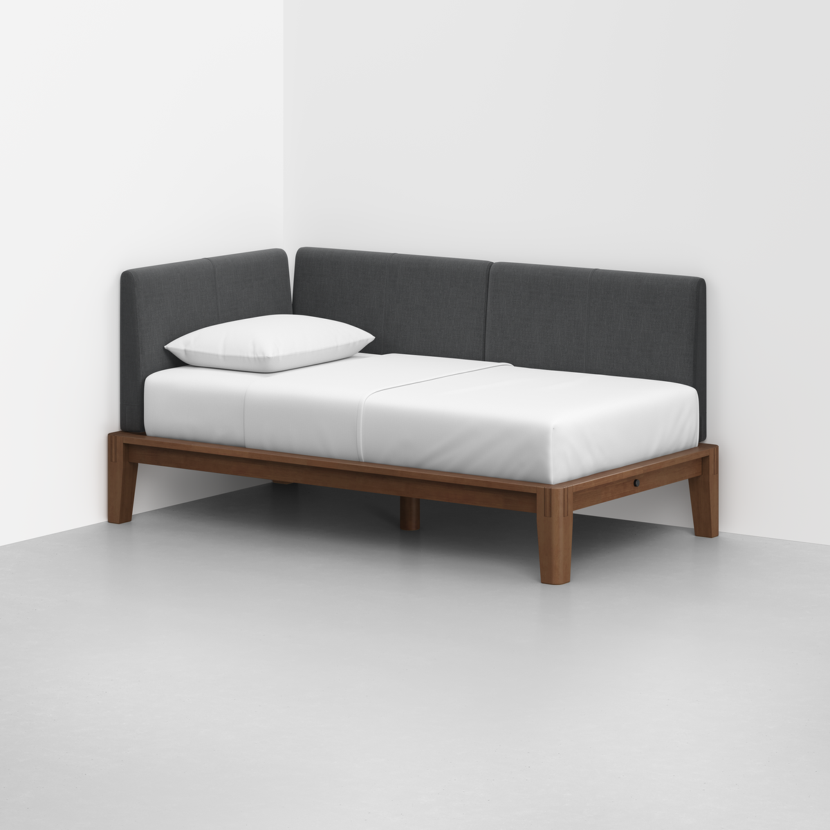 The Classic Daybed features a wooden frame, white mattress, single white pillow, and dark gray upholstered backrest, set in a white room with a light gray floor.
