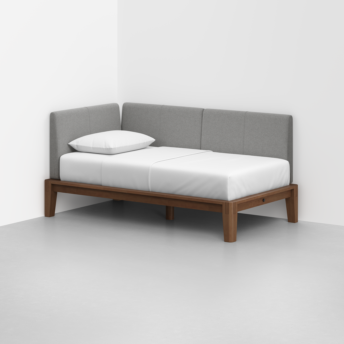 The Classic Daybed features a wooden frame, white mattress, single white pillow, and light gray upholstered backrest set in the corner of a minimalist room with white walls and a light gray floor.