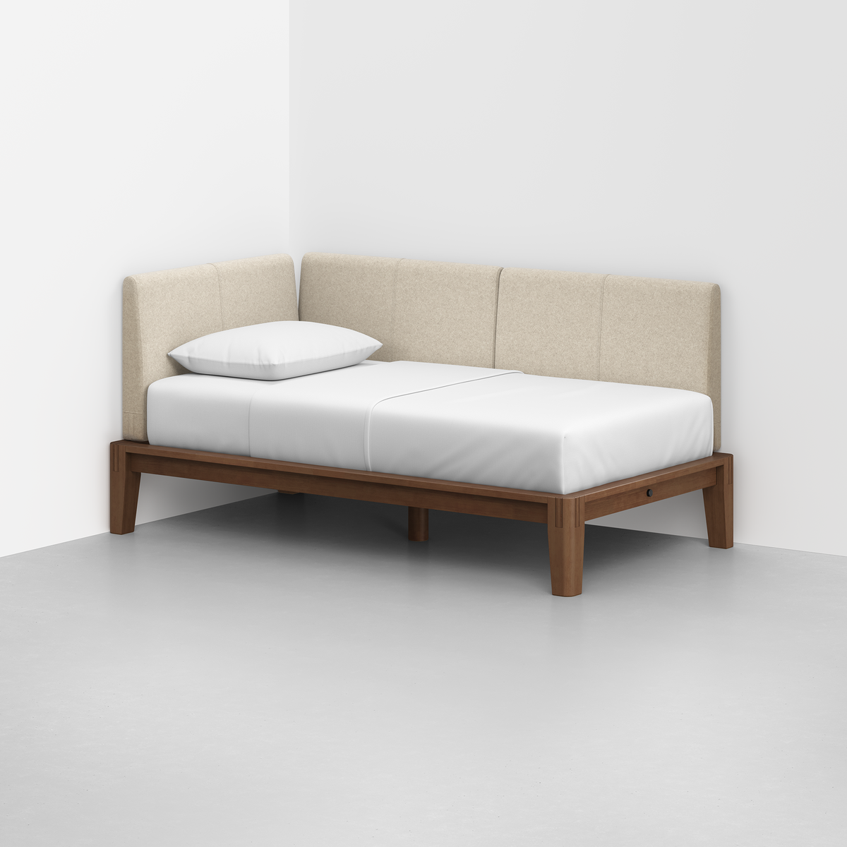 The Classic Daybed features light beige upholstered back and side panels, a single white pillow, and a wooden frame, set in a minimalist, light-colored room with plain walls and floor.