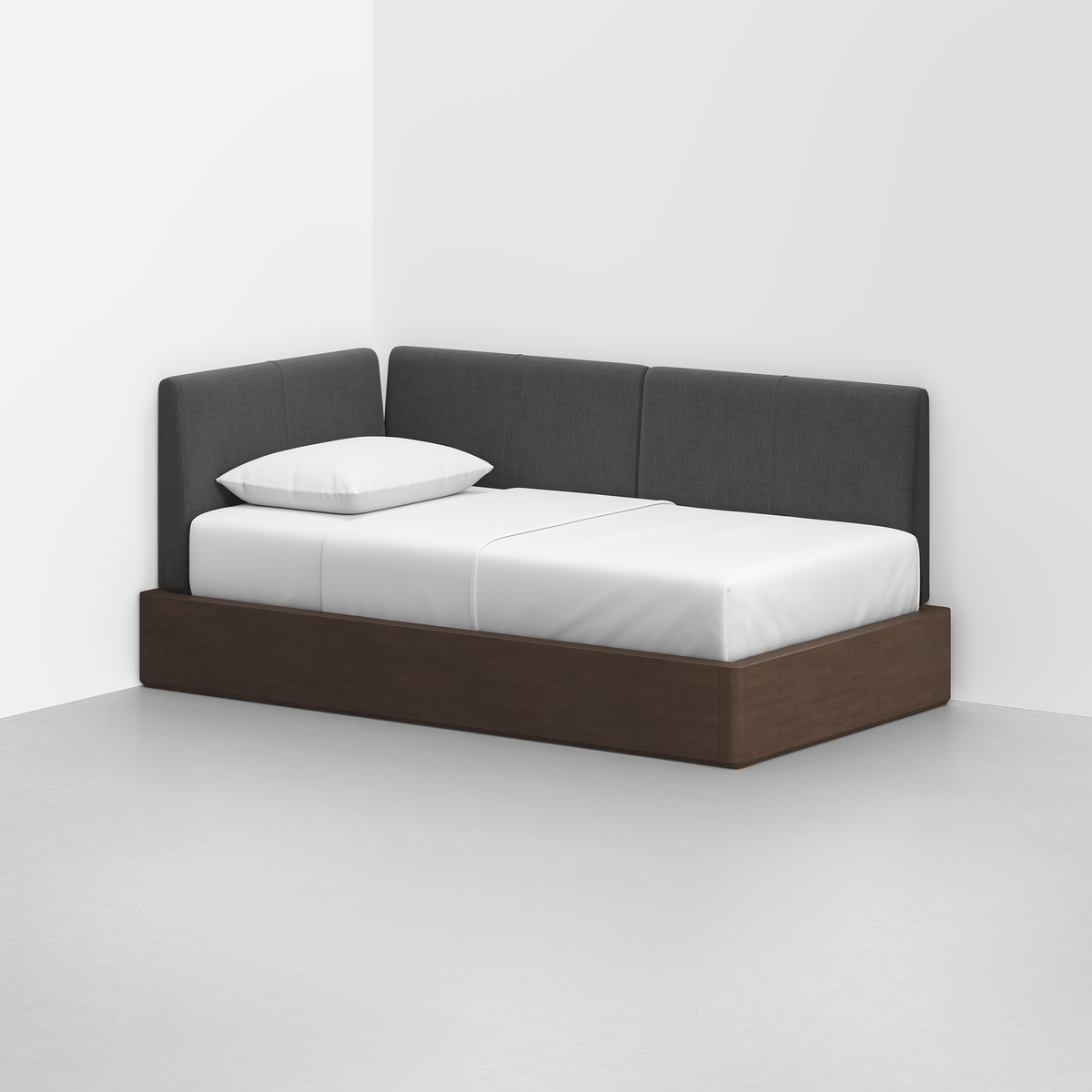 The Essential Daybed features a dark wooden frame and dark gray upholstered backrest, set in a white room with a white mattress, pillow, and bedding.
