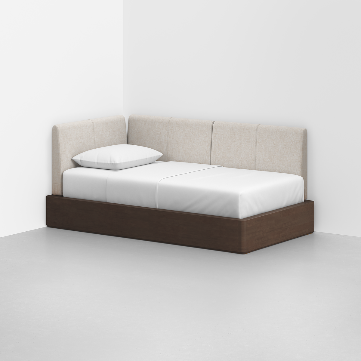 The Essential Daybed, featuring a dark wooden frame and light beige upholstered backrests, sits in the corner of a minimalist white room with a white mattress and single white pillow.