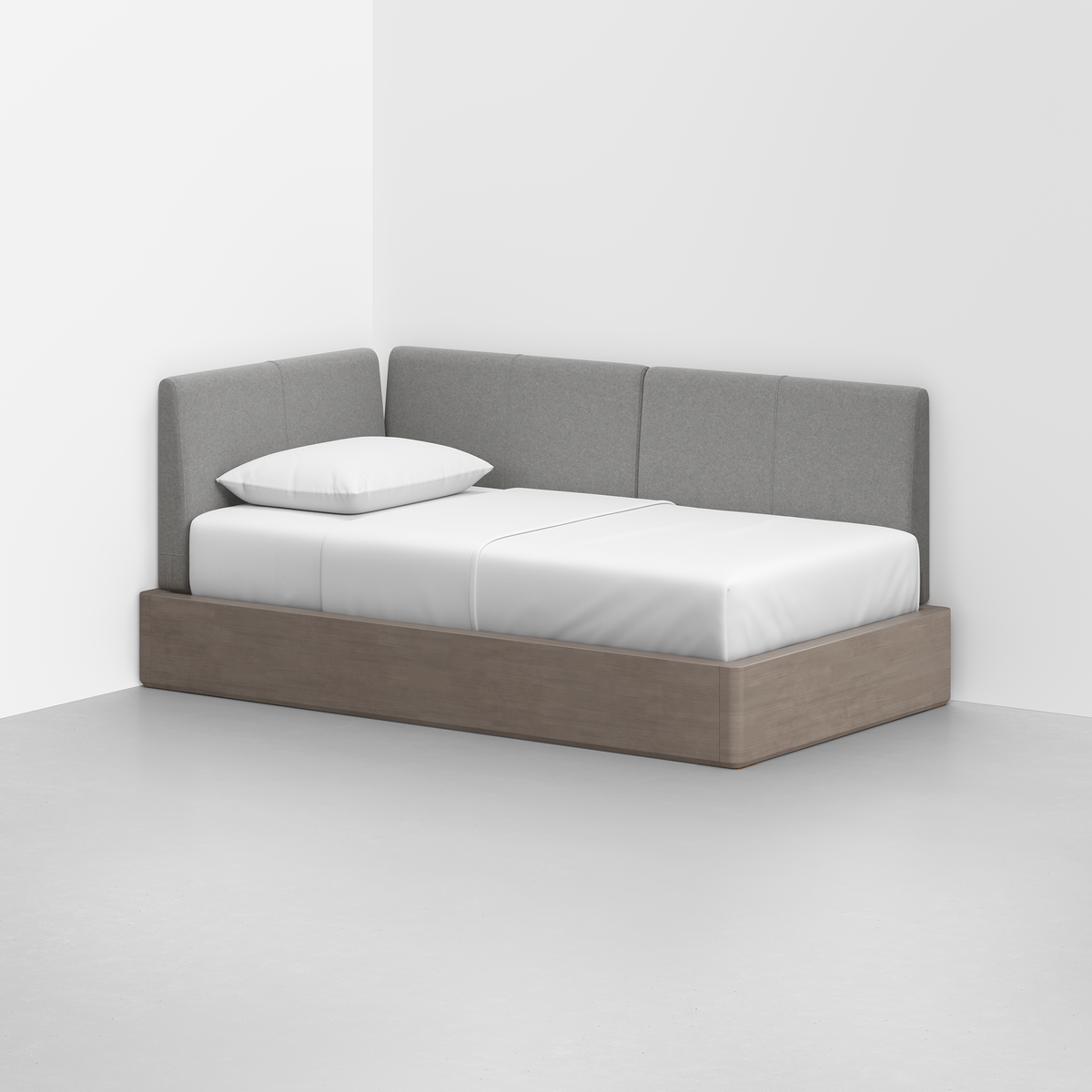 The Essential Daybed, featuring a light wood frame and gray upholstered backrests, is set in the corner of the room. It is dressed with a white sheet and a single white pillow for a clean, minimalist look.