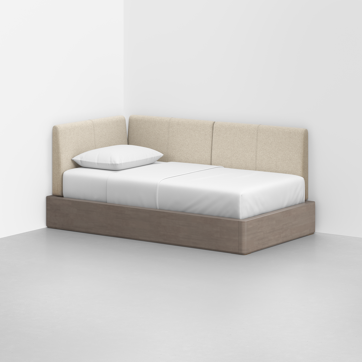 The Essential Daybed, featuring a beige upholstered backrest and wooden base, sits in a minimalist corner, neatly arranged with white bedding and a single white pillow.