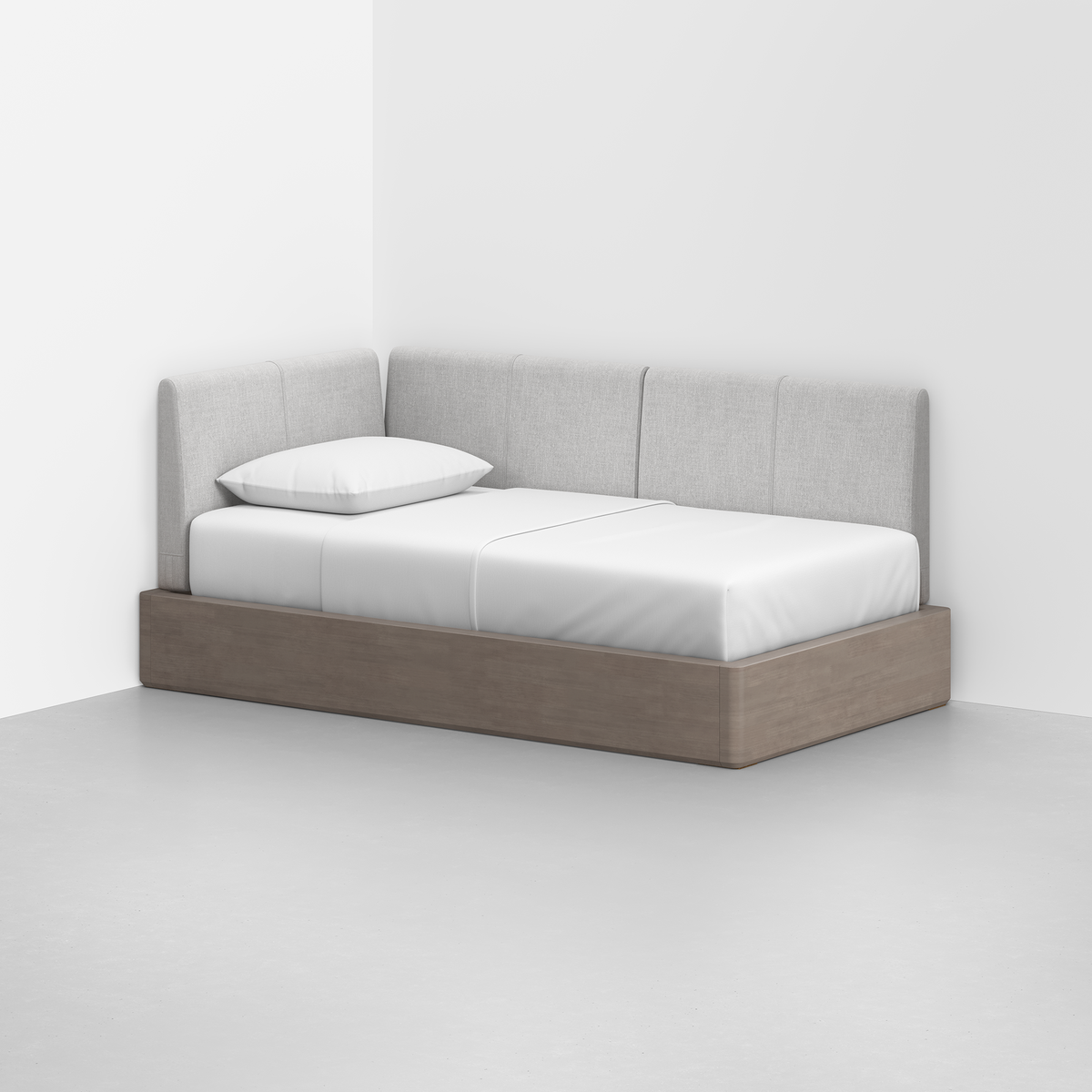 The Essential Daybed with a light wood frame and light gray upholstered back and sides sits in the corner of a minimalist room, neatly made with white bedding and a single white pillow.