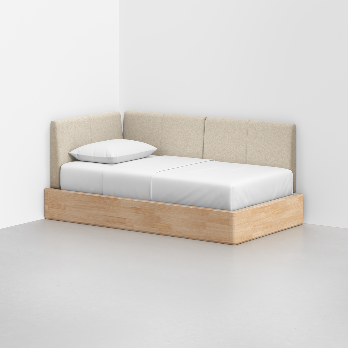 The Essential Daybed features a light wood frame, beige upholstered back and sides, and a crisp white mattress with pillow, set in the corner of a minimalist room.