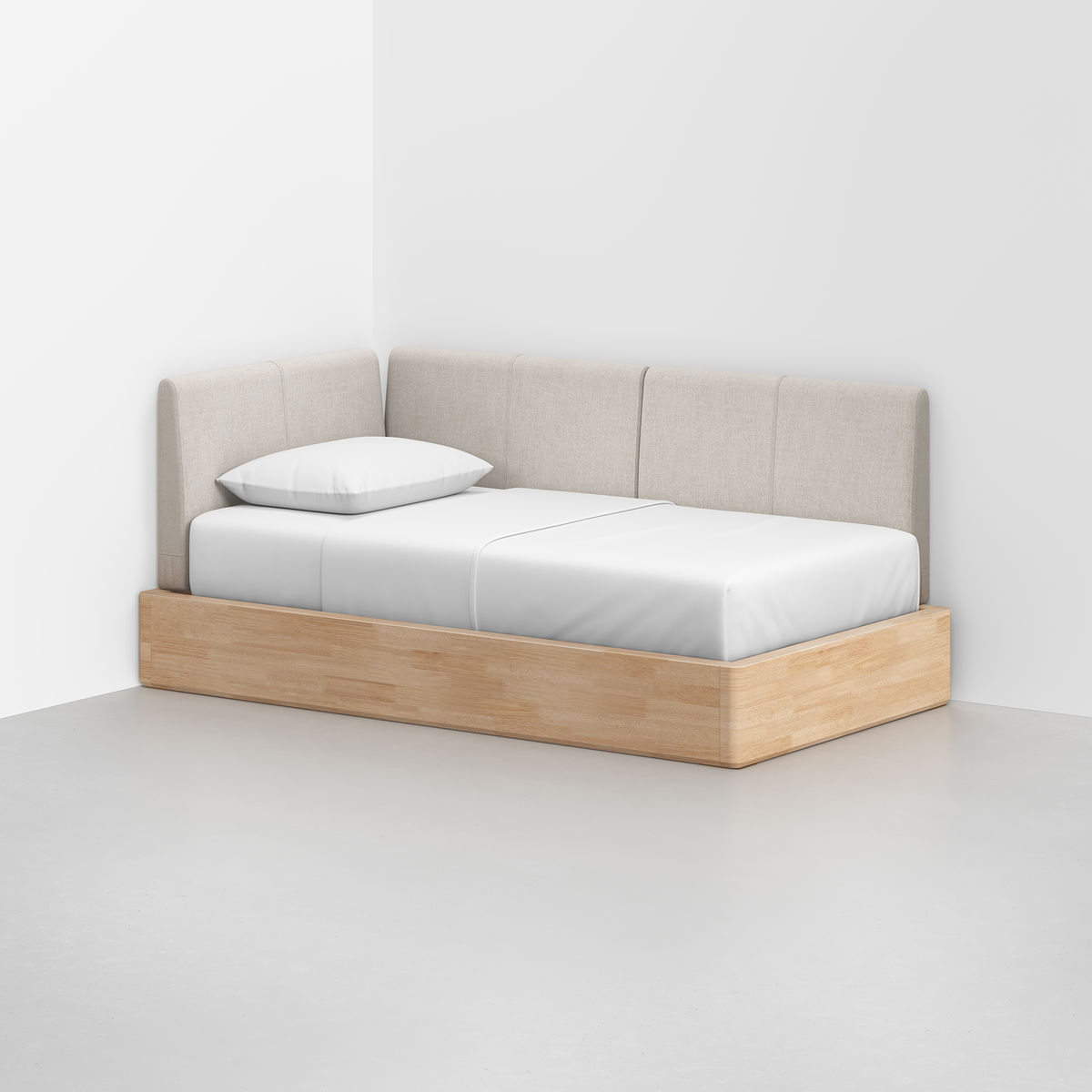 The Essential Daybed features a minimalist design with light beige upholstered back and side panels, white bedding, a single pillow, and a light wood frame, placed in a white room corner with a smooth light gray floor.