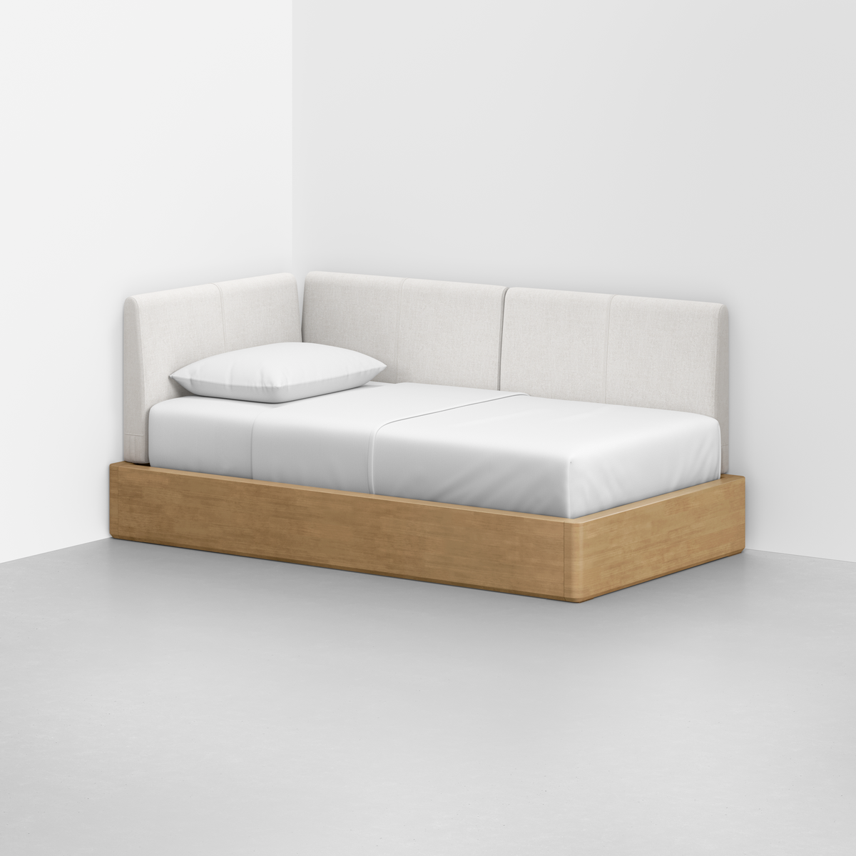 The Essential Daybed features a minimalist light wood frame with white cushioned back and side panels, plus a white mattress and pillow, all set against a plain white wall and floor.