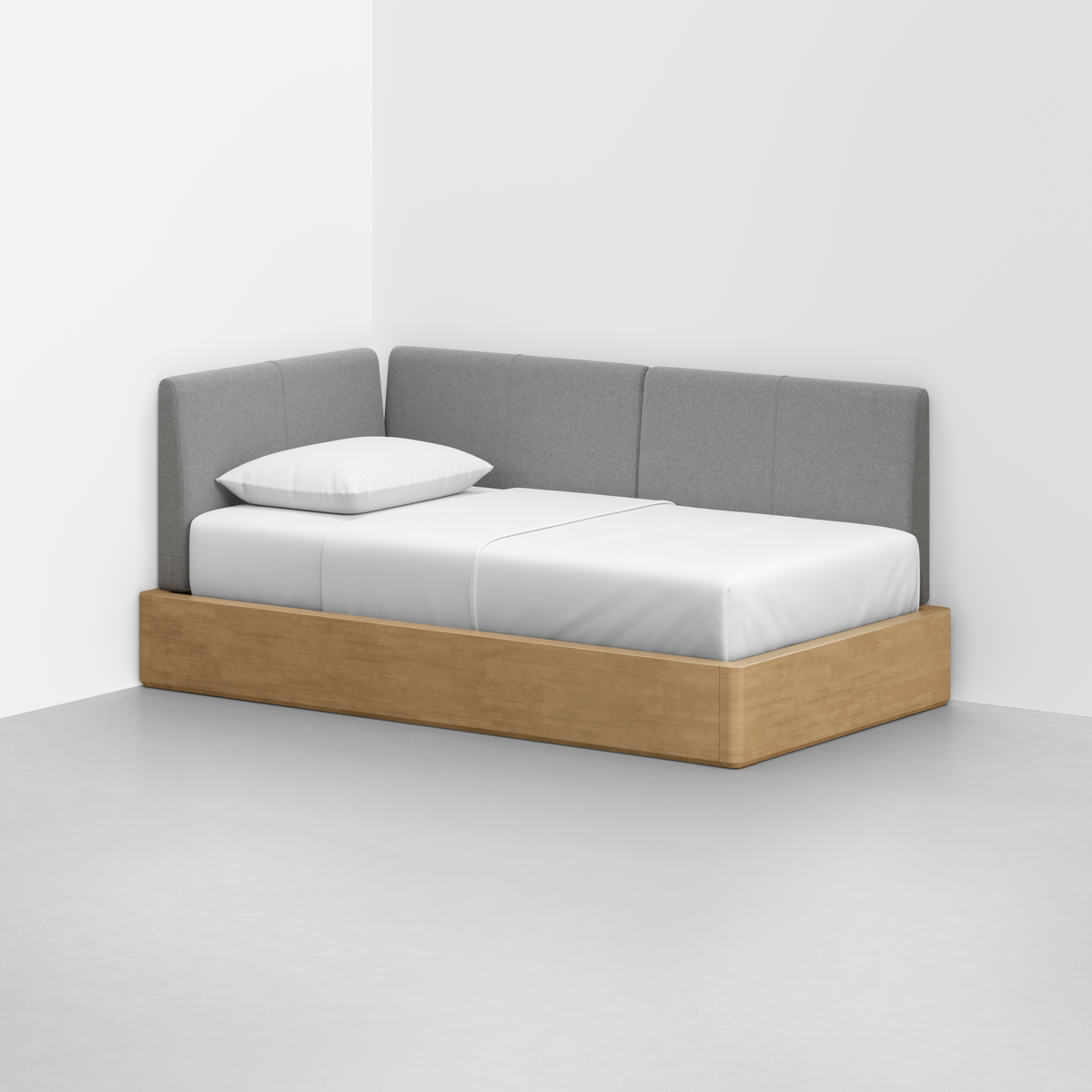 The Essential Daybed features a light wood base, gray upholstered back and side panels, and a white mattress with a single white pillow, perfectly suited for a minimalist room with white walls and a gray floor.