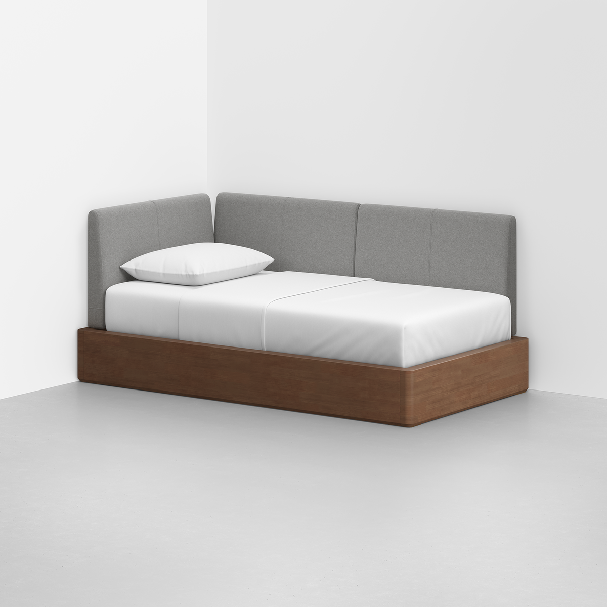 The Essential Daybed features a wooden frame and light gray upholstered backrests, shown in the corner of a white room with white bedding and a single pillow.