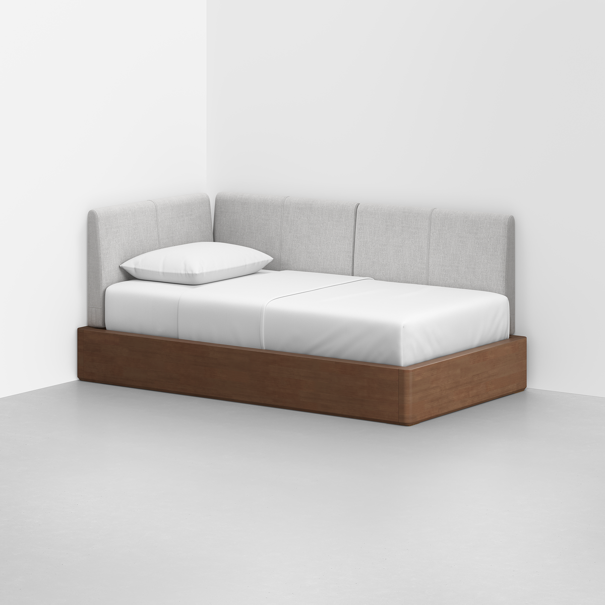 The Essential Daybed features a wooden frame with light gray upholstered back and side panels, perfectly suited for a minimalist room with white walls and a gray floor.