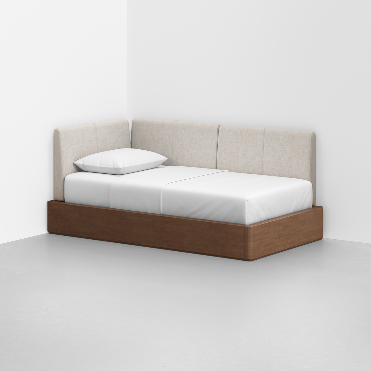 The Essential Daybed features a wooden base, white mattress, single pillow, and beige upholstered back and side panels, perfectly suited for the corner of a minimalist room with white walls and a light gray floor.