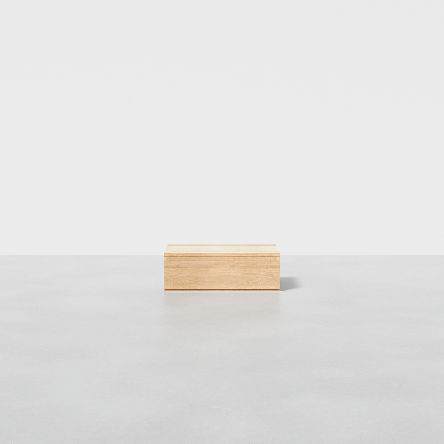 The Nest Nightstand Low, a small rectangular wooden piece, sits alone on a smooth light gray surface with a plain white background.
