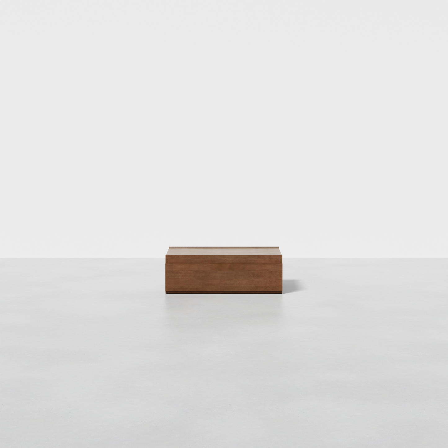 The Nest Nightstand Low, a rectangular wooden piece, sits centered on a smooth light gray floor against a plain white background in a minimalist, empty setting.