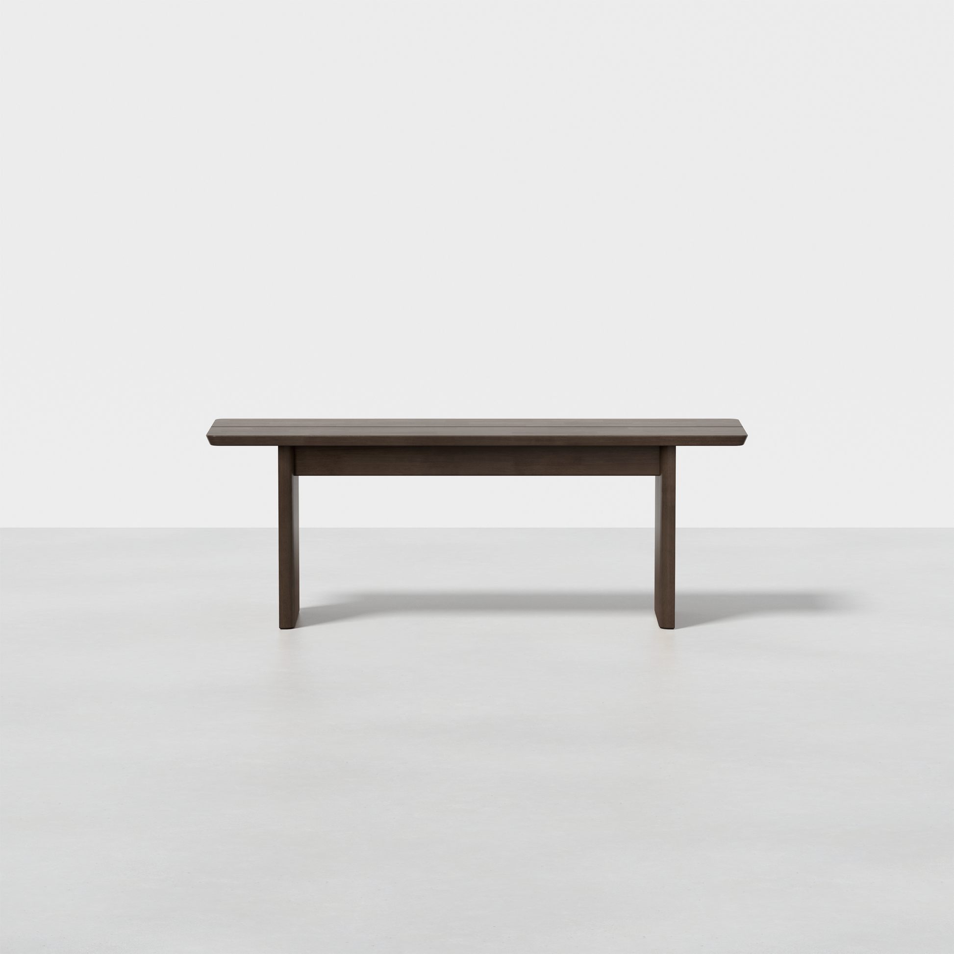 The Pillar Bench features a modern, minimalist wooden design with clean lines and a dark finish, shown on a light gray floor against a plain white background. No cushions or decorative features are present.