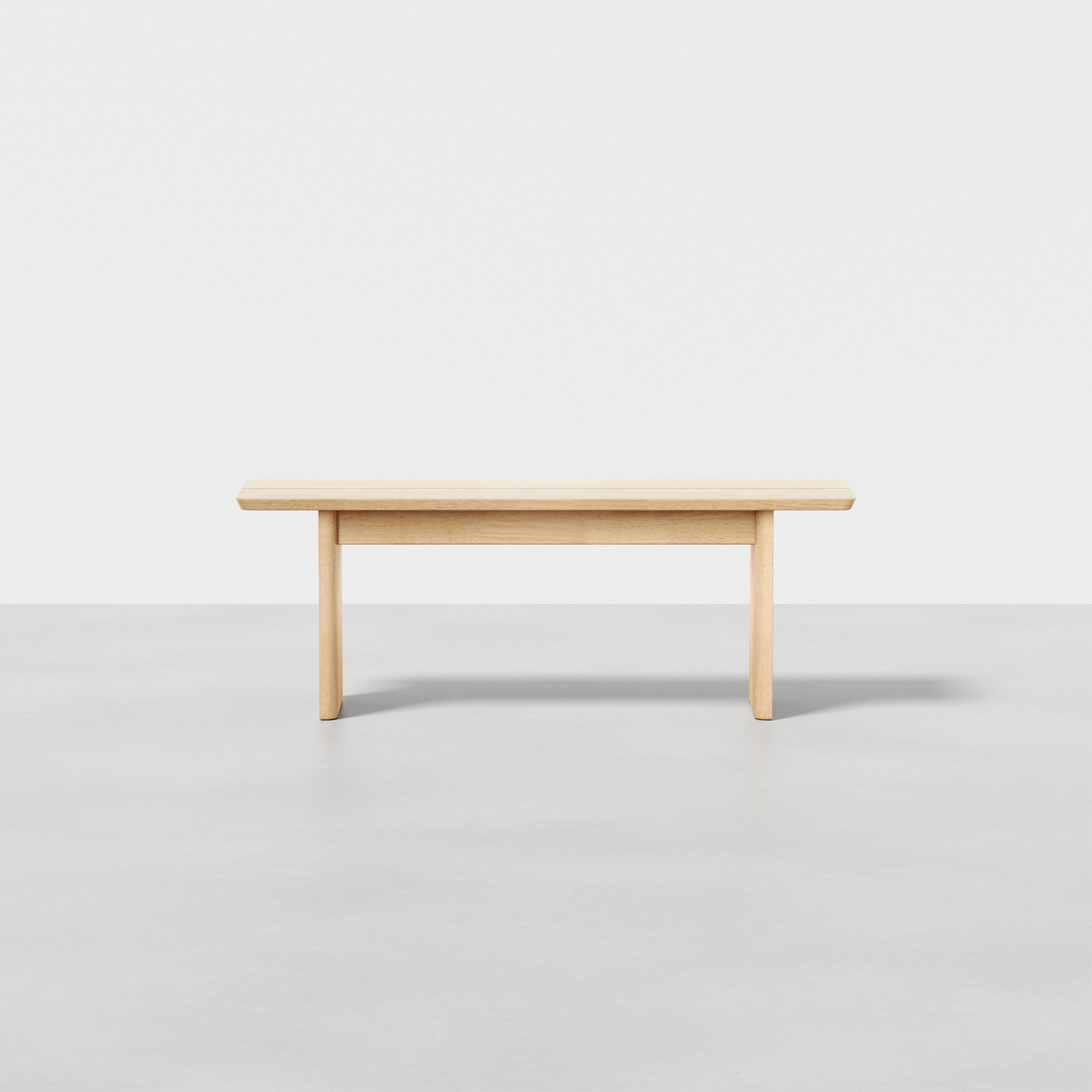 The Pillar Bench features clean lines and a light natural wood finish, shown against a plain white background on a smooth gray floor.