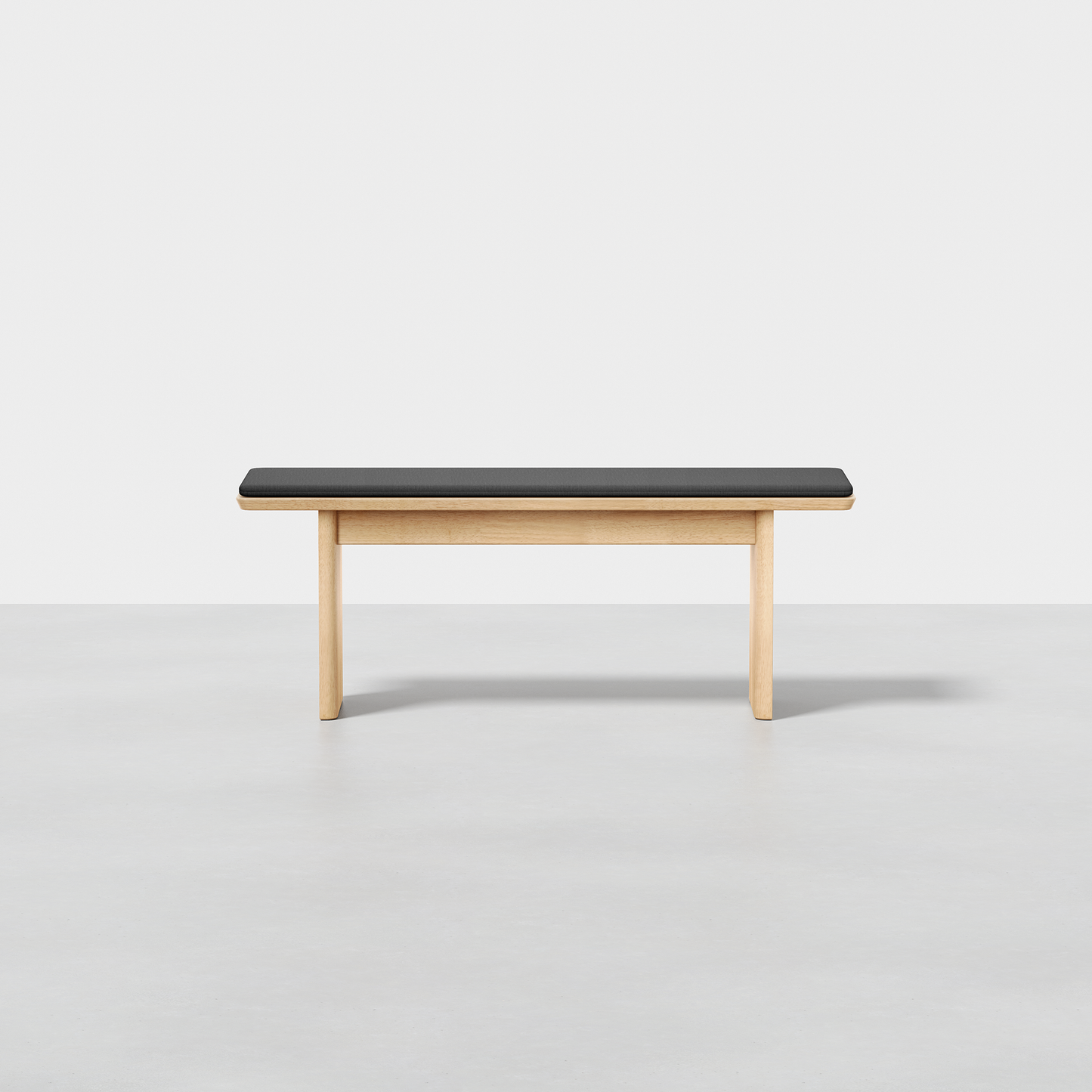 The Pillar Bench features a minimalist design with a black cushioned seat and light wood legs, shown against a plain white background.