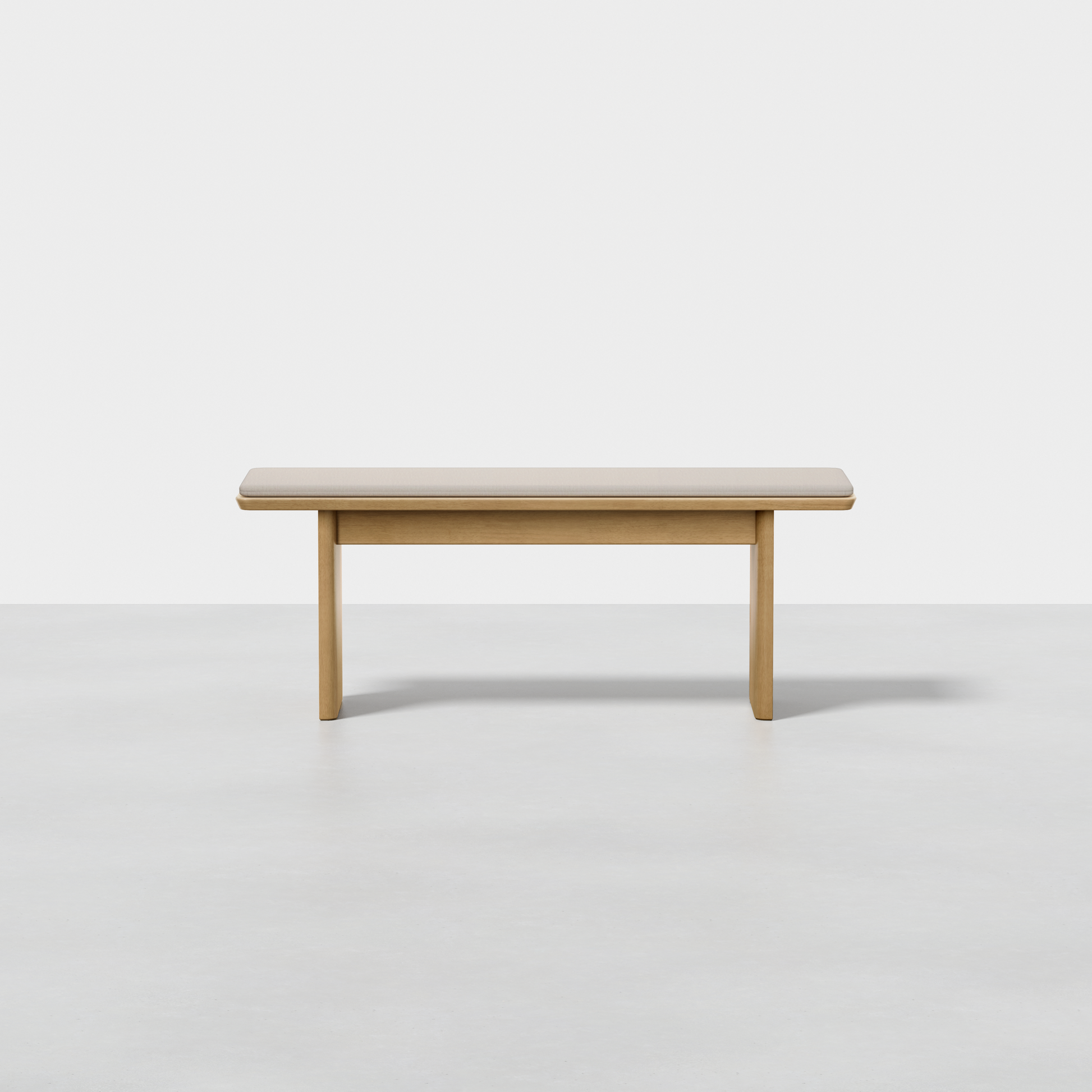 The Pillar Bench is a simple rectangular wooden bench with a smooth surface and four sturdy legs, shown on a light gray floor against a plain white background.