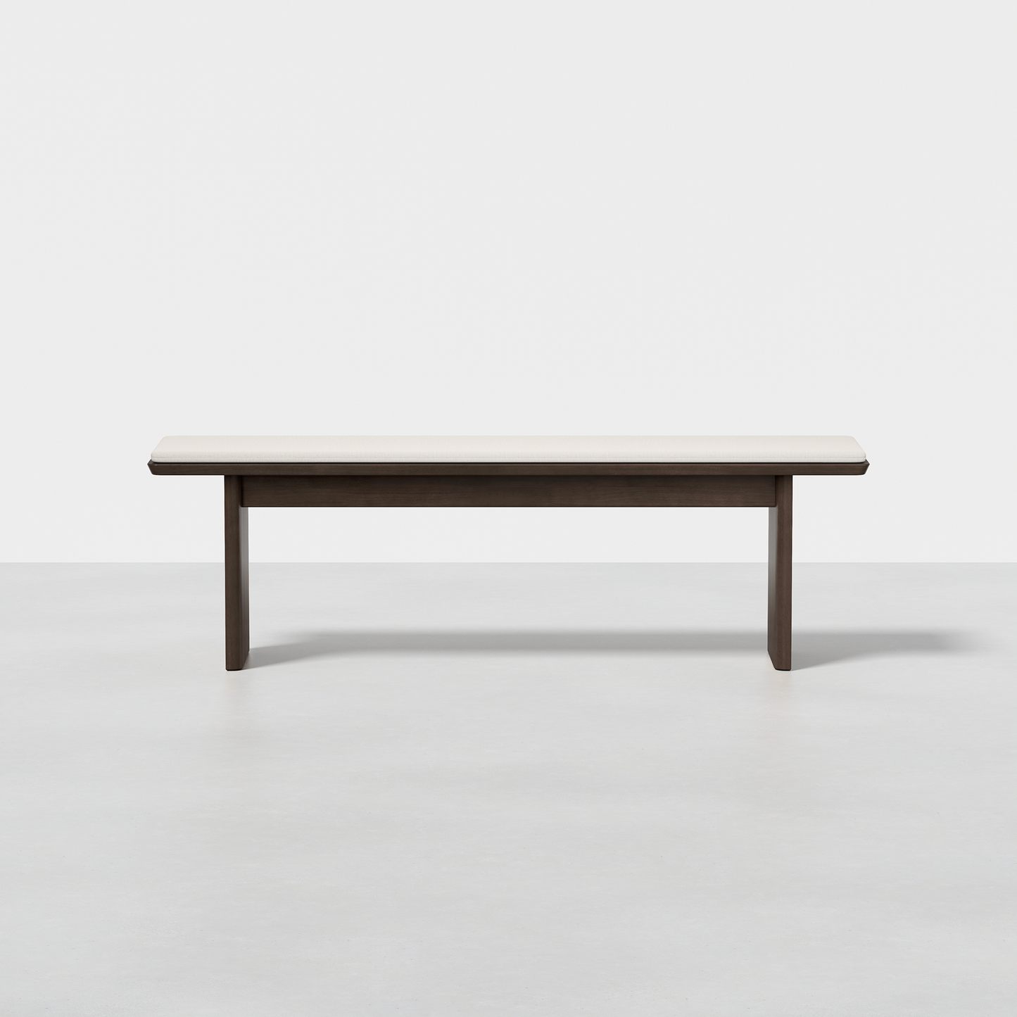 The Pillar Bench features a minimalist design with a light wood seat and dark legs, displayed on a smooth light gray floor against a plain white background.