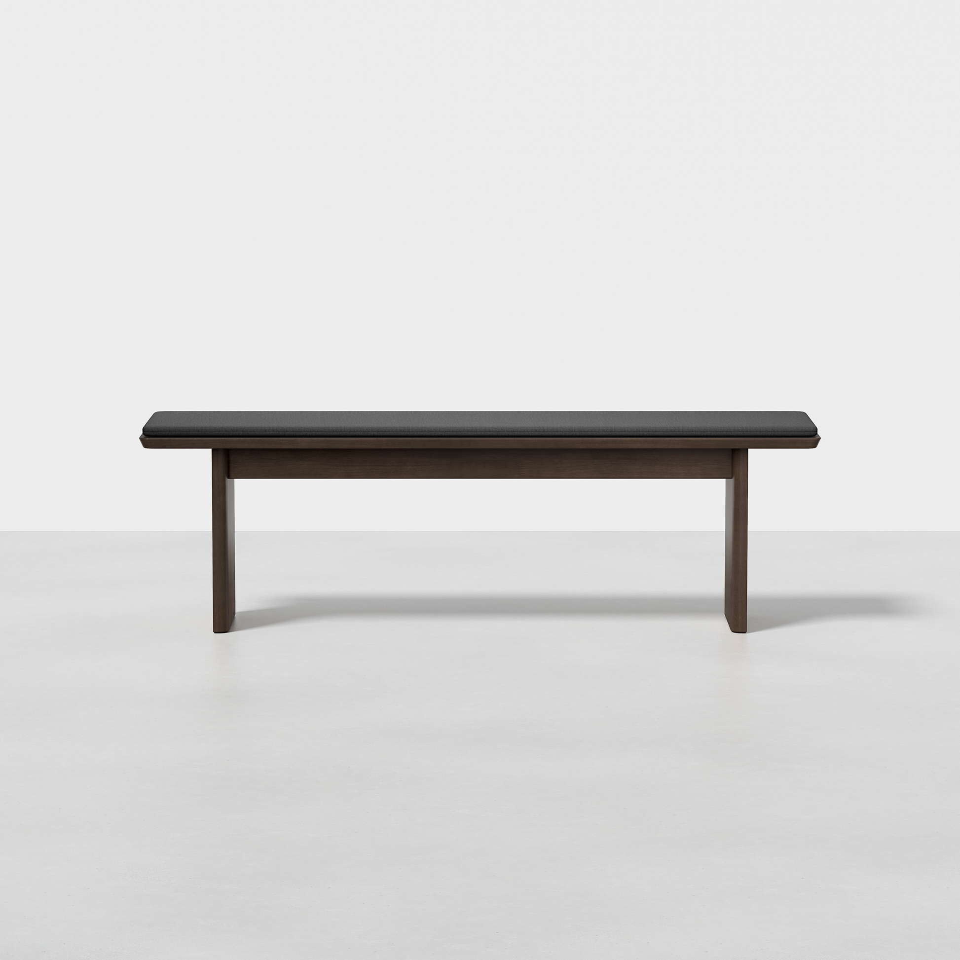 The Pillar Bench features a minimalist wooden design with straight legs and a dark cushioned seat, shown against a plain white background.