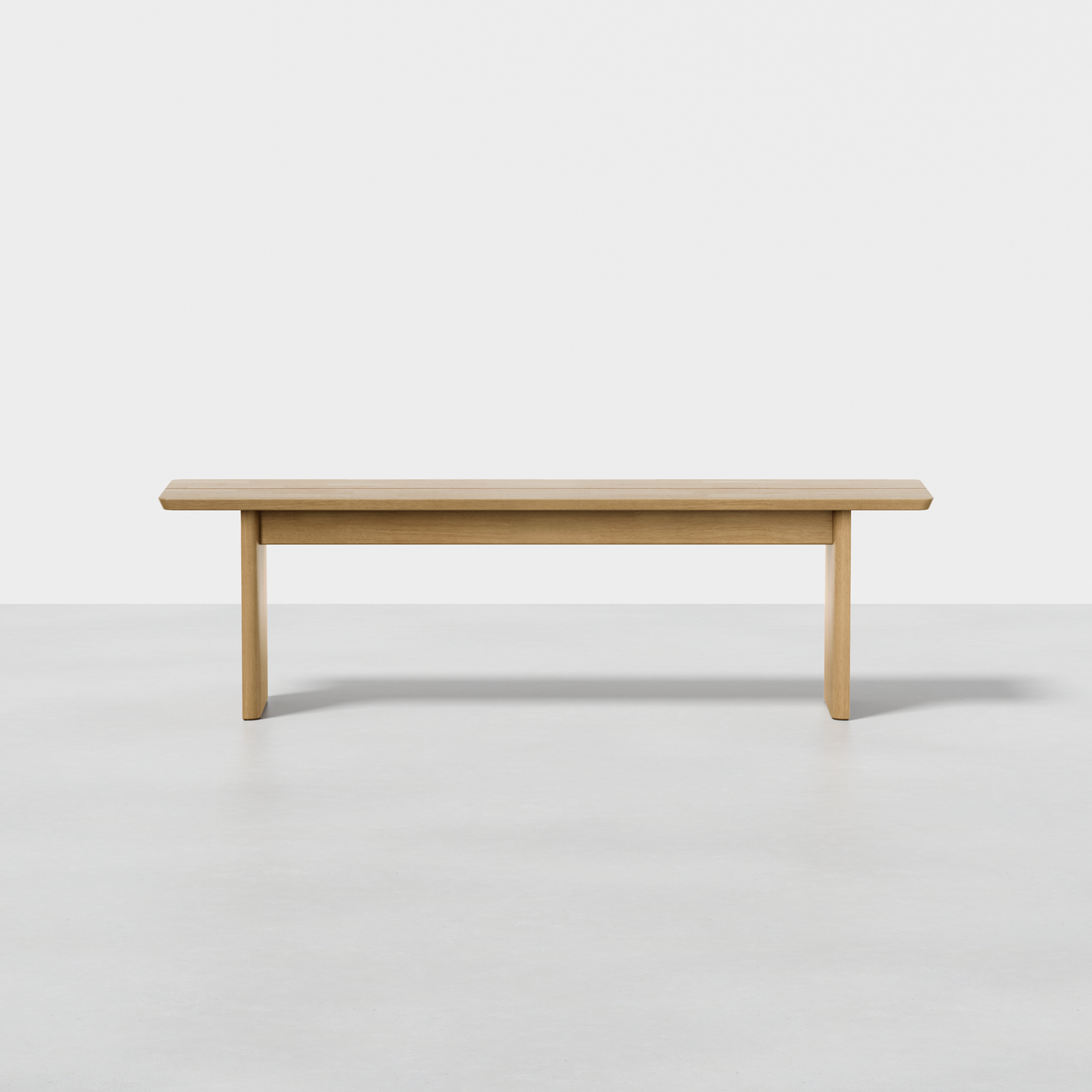 The Pillar Bench, a minimalist piece with light wood, clean lines, and rectangular legs, sits on a smooth light gray floor against a plain white background.