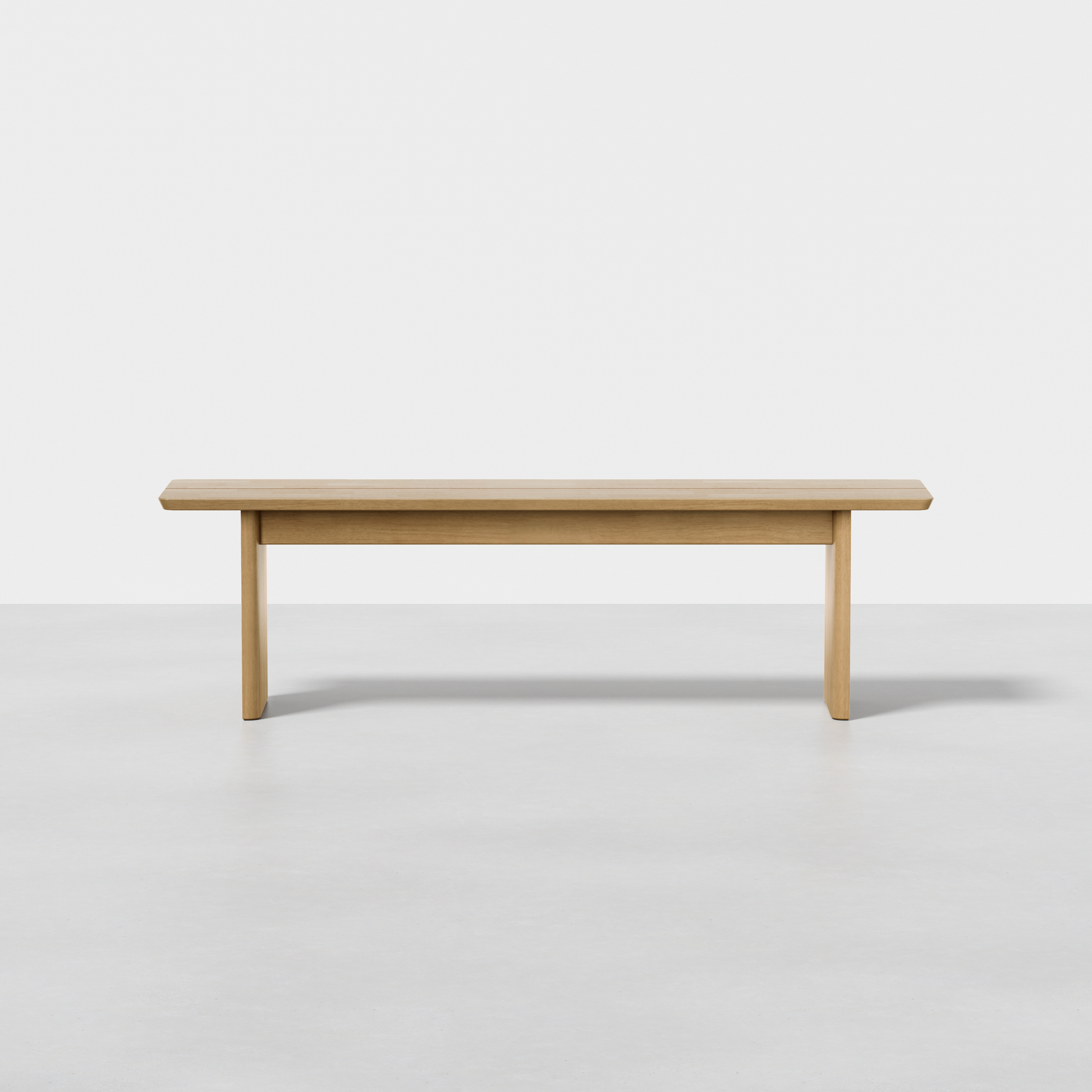 The Pillar Bench, a minimalist piece with light wood, clean lines, and rectangular legs, sits on a smooth light gray floor against a plain white background.